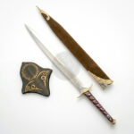 Fantasy-style sword set displayed on a white background featuring a polished silver blade with engraved details, a maroon wrapped handle with gold accents, a brown decorative scabbard with ornate gold fittings, and a matching shield-shaped display piece with engraved patterns.